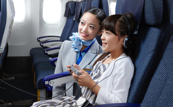 機内エンターテインメントを視聴する少女と客室乗務員